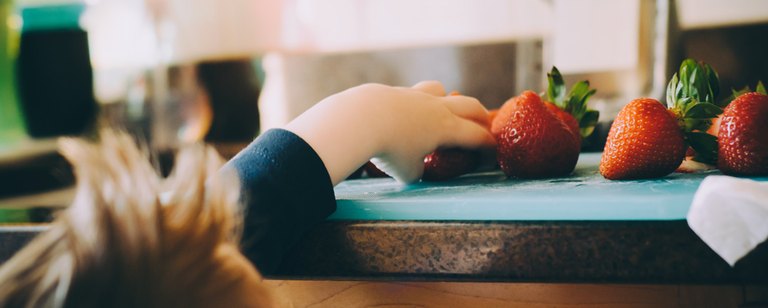 Kinderhand greift nach frischen Erdbeeren, die auf der Küchenablage liegen