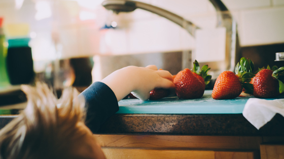 Kinderhand greift nach frischen Erdbeeren, die auf der Küchenablage liegen 