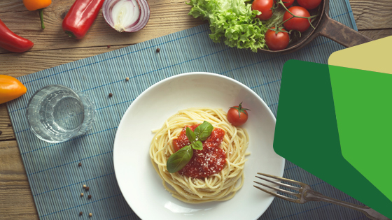 Tischoberfläche mit einem Teller Spaghetti, einem Wasserglas und dekorativem Gemüse 