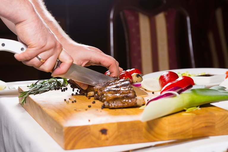 Ein Stück Fleisch wird auf einem Brett in Scheiben geschnitten 