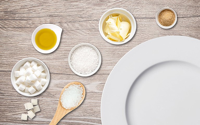 Salz, Fett und Zucker in verschiedenen Gefäßen um einen leeren Teller angeordnet